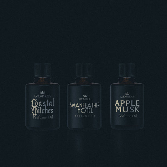 Three perfume bottles labeled 'Coastal Witches', 'Swanfeather Hotel', and 'Apple Musk' on a dark background.
