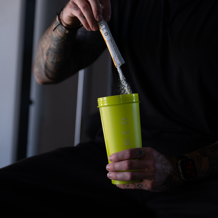 Person pouring supplement powder into a Volt KAGED shaker bottle in a low-lit workout setting
