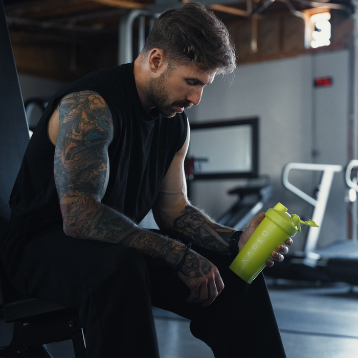 Three-quarter view of Volt 28oz shaker bottle showcasing KAGED logo and flip-top lid held by man in gym