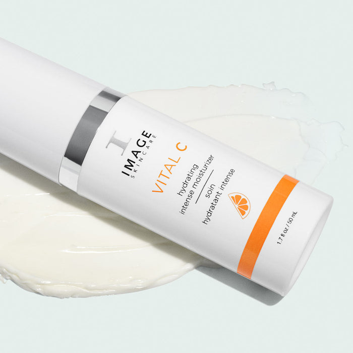 VITAL C hydrating intense moisturizer | IMAGE Skincare bottle lying on a light surface with cream texture spread underneath, featuring orange accents and skin care branding.