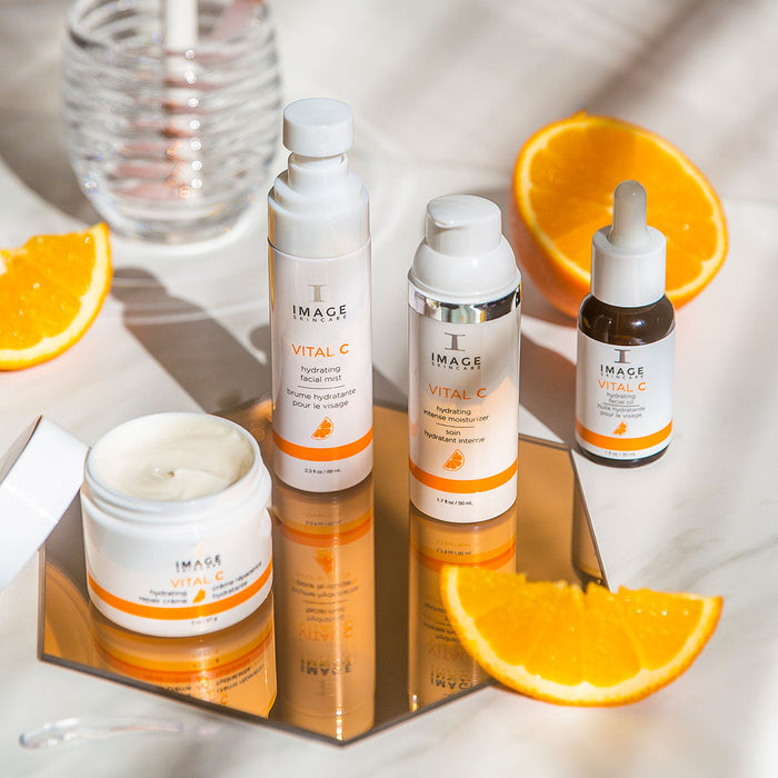 VITAL C hydrating intense moisturizer | IMAGE Skincare displayed with matching facial cream, serum, and hydrating facial mist surrounded by fresh orange slices on a reflective surface.