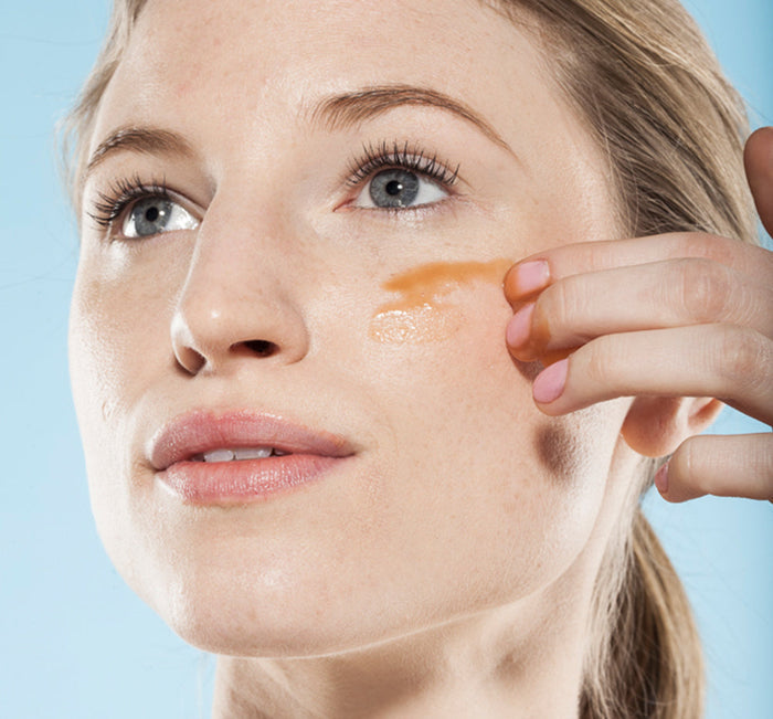 Close-up of a woman applying Wine Down® Overnight Super Antioxidant Recovery Serum | Farmhouse Fresh to her cheek, highlighting skincare and evening skin tone.