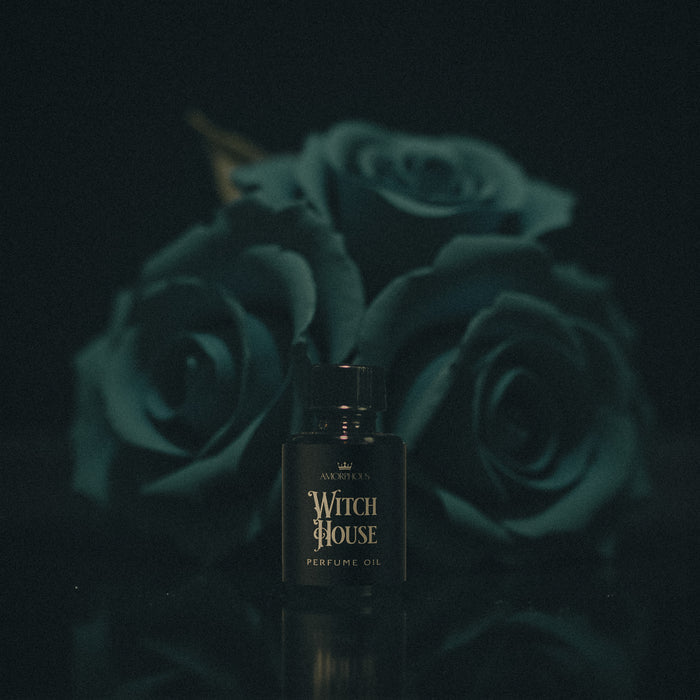 Perfume bottle labeled 'Witch House' with teal roses in the background